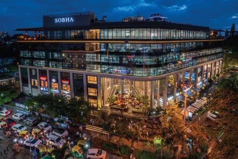 Tall blue building with many balconies lit up at night with palm trees in front